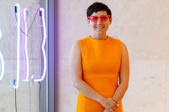 Liss LaFleur in the Nasher Public Gallery in an orange dress and neon glasses
