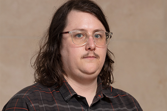 A man with glasses, shoulder length hair, and dark shirt