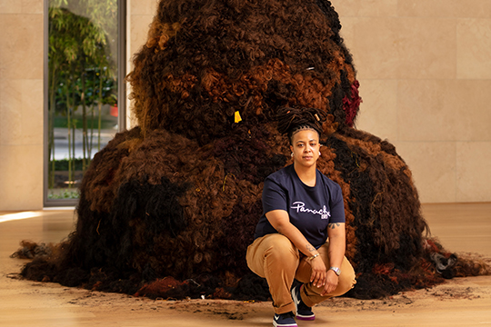 A woman kneeling in front of large hair sculpture