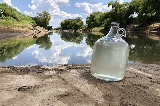 jug of water sitting by a river with blue sky and clouds