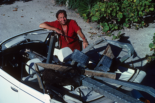 Artist Robert Rauschenberg sits in a convertible surrounded by found objects
