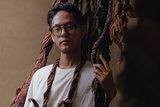 the artist posed next to his woven sculptural creation