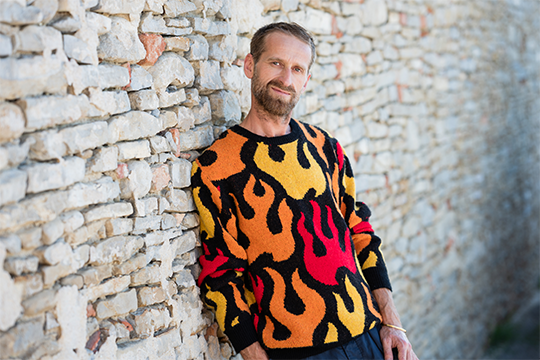 the artist in a sweater with colorful flames on it
