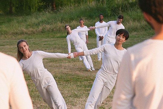 Dancers in white hold hands in a field