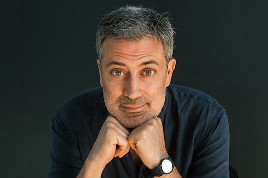 Left: Andrea Bajani, a man with short salt and pepper hair, rests his hands on his chin. 
