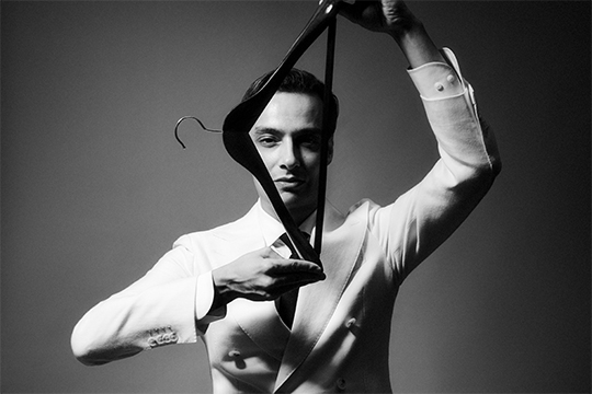 Black and white photo of Mohamed Benchellal, a man in a white suit with dark hair holding a clothes hanger