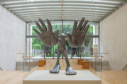 Large steel sculpture of a figure holding out two enlarged hands in front of them.