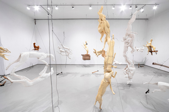 A group of plaster, rubber, and polyurethane sculptures depicting animal forms, suspended with wire and weighted by found objects, displayed in a white walled gallery space. 