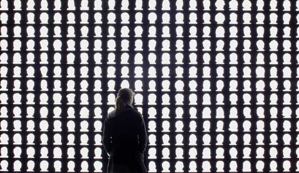 Viewer examines artwork of white silhouetted of heads on an illuminated black background, entitled The Geometry of Conscience, 2010 by Alfredo Jaar