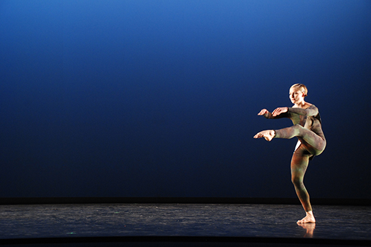 A dancer holds a pose against a dark background