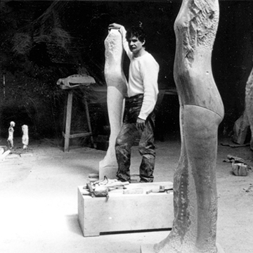 Artist Manuel Neri standing between plaster figure sculptures