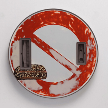 Image of a wall-mounted sculpture resembling a keep out sign with an image of a pastry on it.
