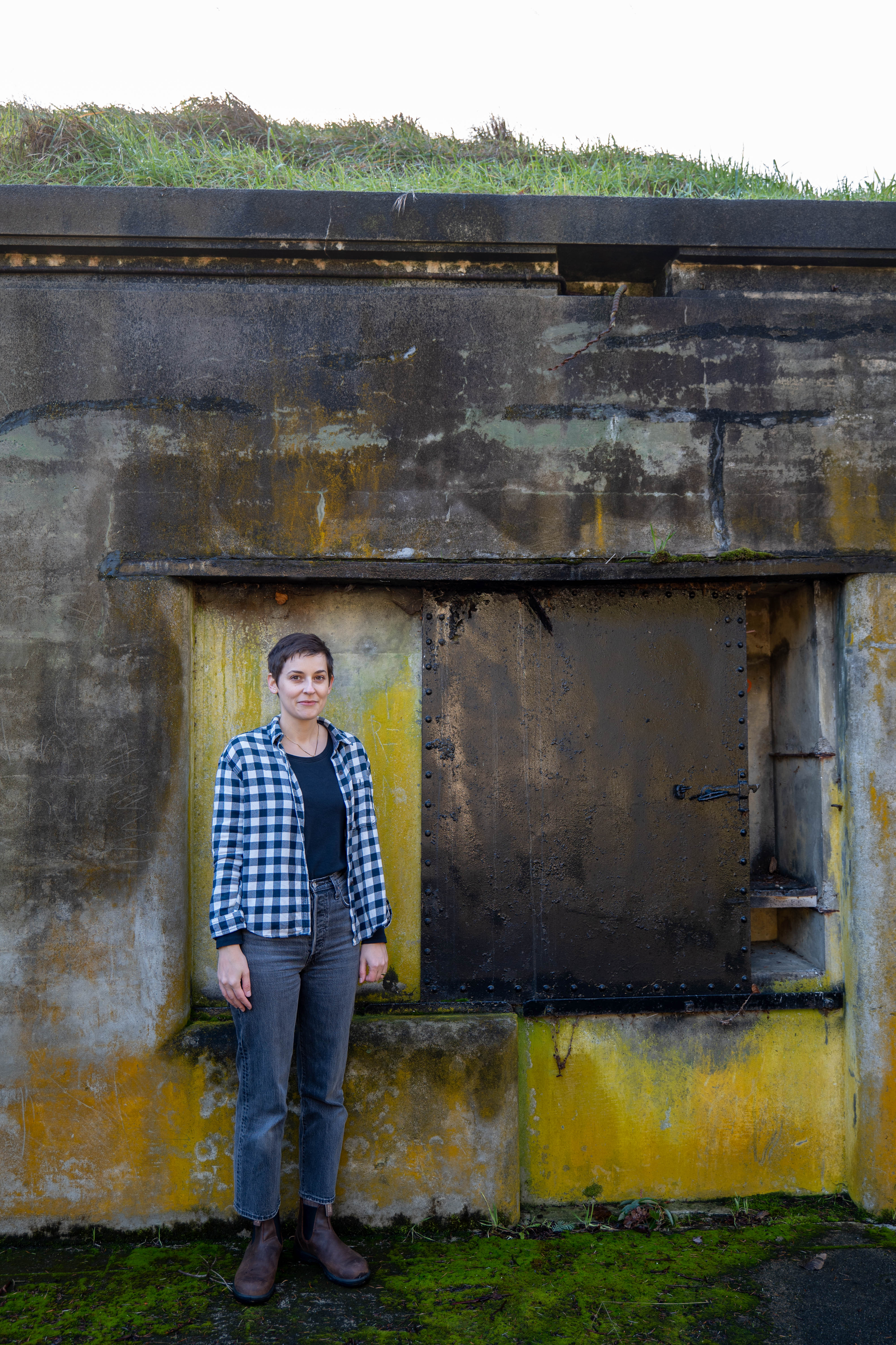 A woman with short dark hair stands in front of a building A woman with short dark hair stands in front of a building